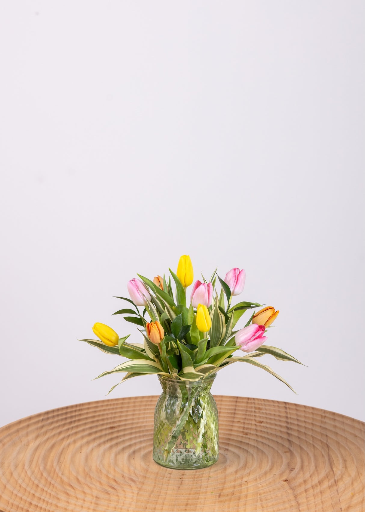 Ten colorful assorted tulips with extra greenery in a small cylinder vase.