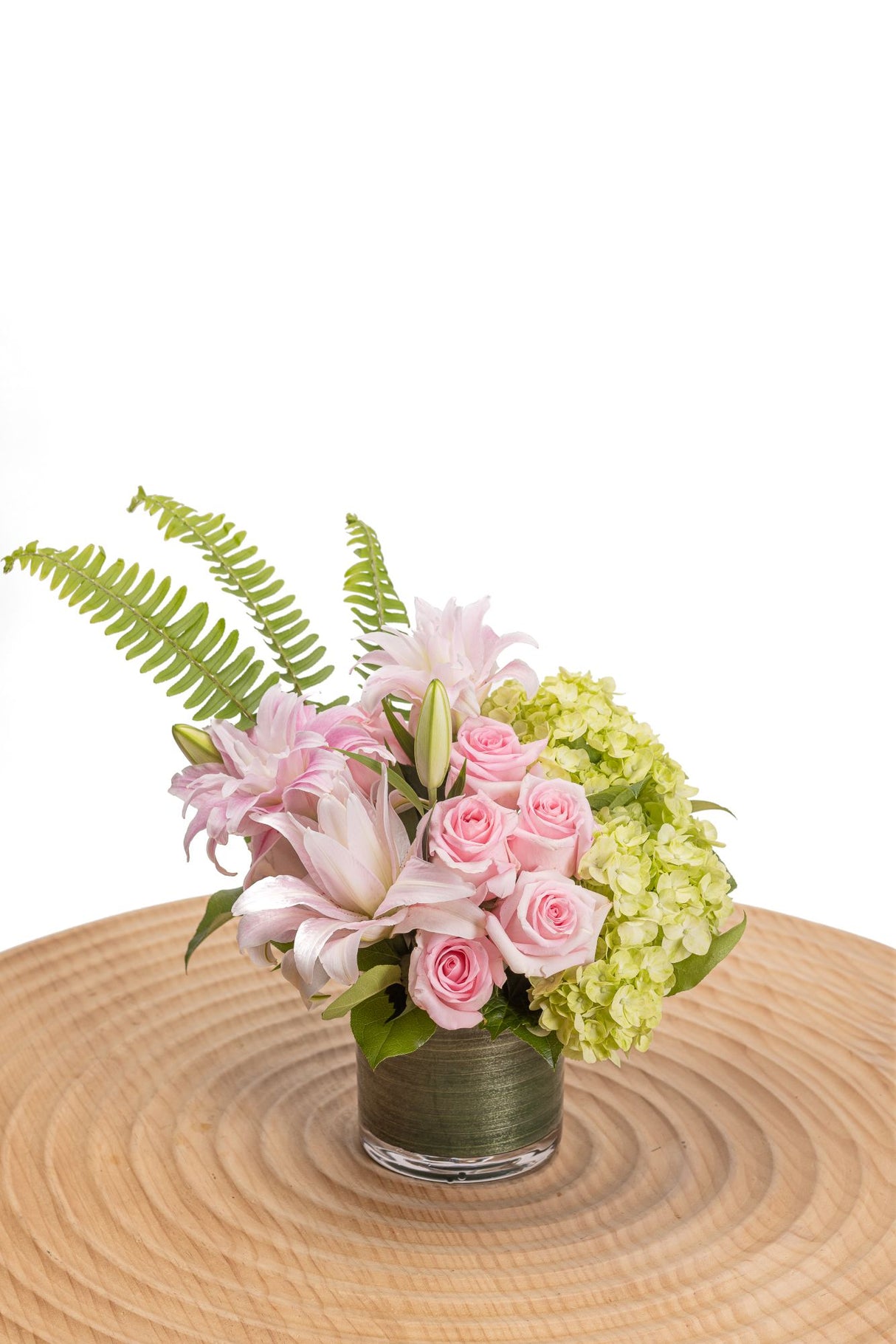 Maximum Preppy Petals features ten pink roses, large green hydrangea, sword ferns, three double rose lilies and two green cymbidium orchids in a glass cylinder vase.