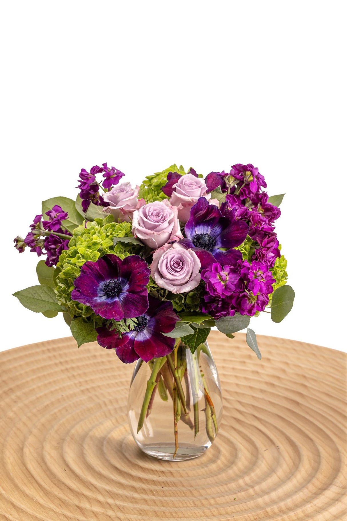 Purple Bliss features lavender roses, purple stock, anemones, dollar eucalyptus and deep green hydrangeas in an elegant glass vase.