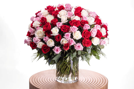 100 Romantic Roses features one hundred roses in red, pink, and white accented with greenery, arranged in a large glass cylinder vase.