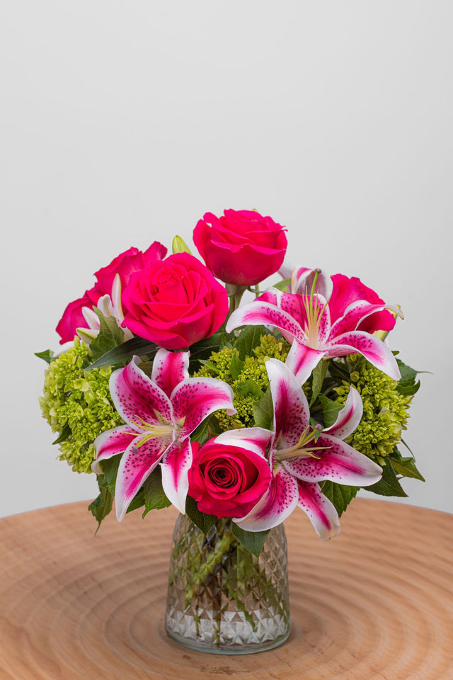 Dearest features six hot pink roses, three starfighter lilies, mini green hydrangeas, and luxe foliage in a small cinch vase.