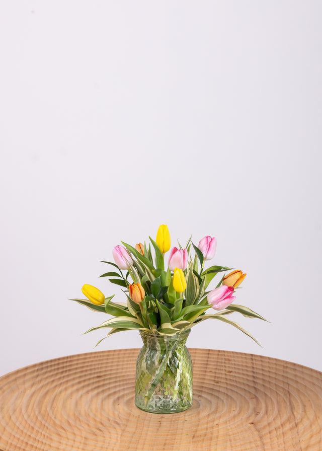 Ten colorful assorted tulips with extra greenery in a small cylinder vase.