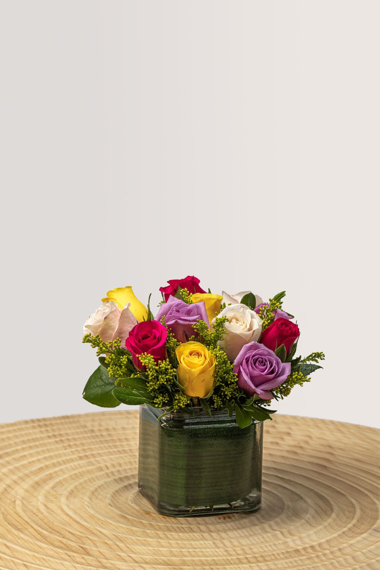 The Elizabeth flower arrangement features yellow, pink, purple, and pink roses with greenery in a cube vase.