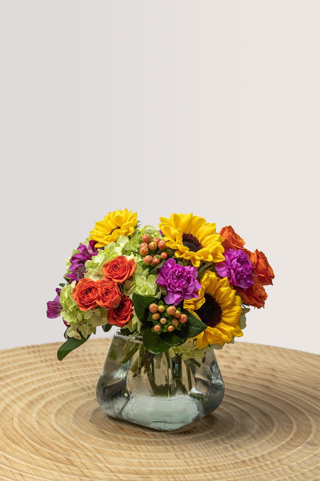 Fun arrangement consisting of purple alstroemeria, lavender carnations, green hydrangea, orange spray rose.