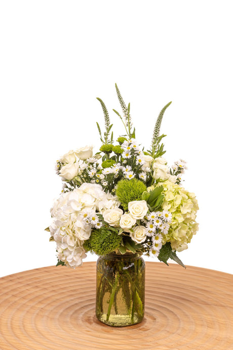 Peridot features green and white hydrangea, spray roses, green trick, button poms, and veronica arranged in a vintage green hammered jar vase.