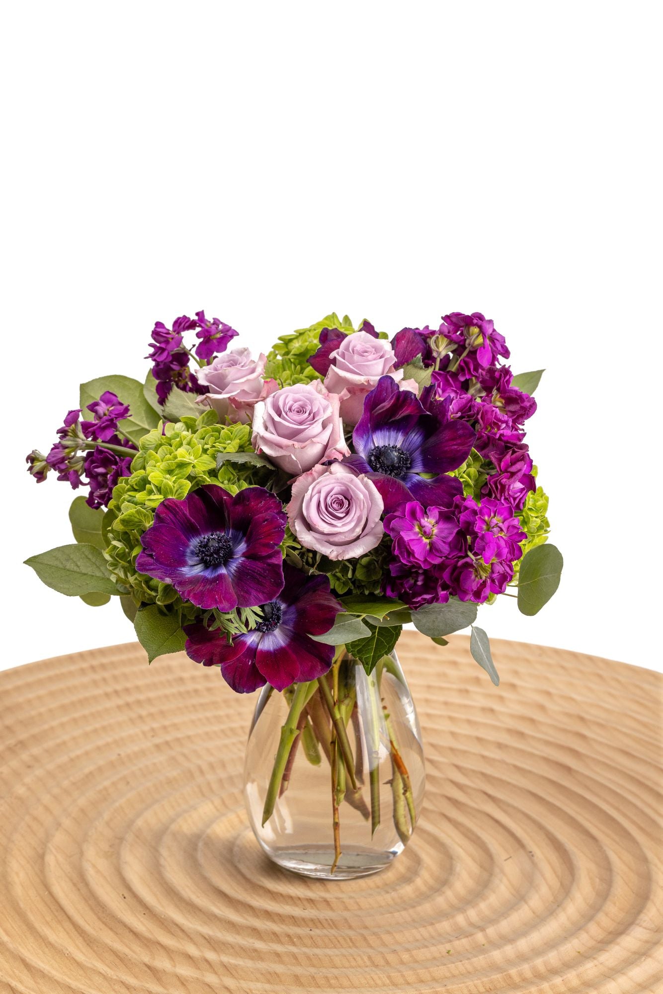 Purple Bliss features lavender roses, purple stock, anemones, dollar eucalyptus and deep green hydrangeas in an elegant glass vase.