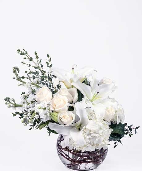 Elegant all-white floral arrangement with hydrangea, lilies, roses, and stock in an 8-inch bubble ball vase