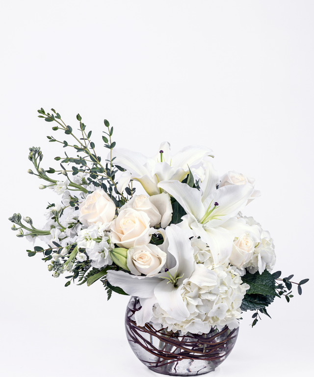 Elegant all-white floral arrangement with hydrangea, lilies, roses, and stock in an 8-inch bubble ball vase
