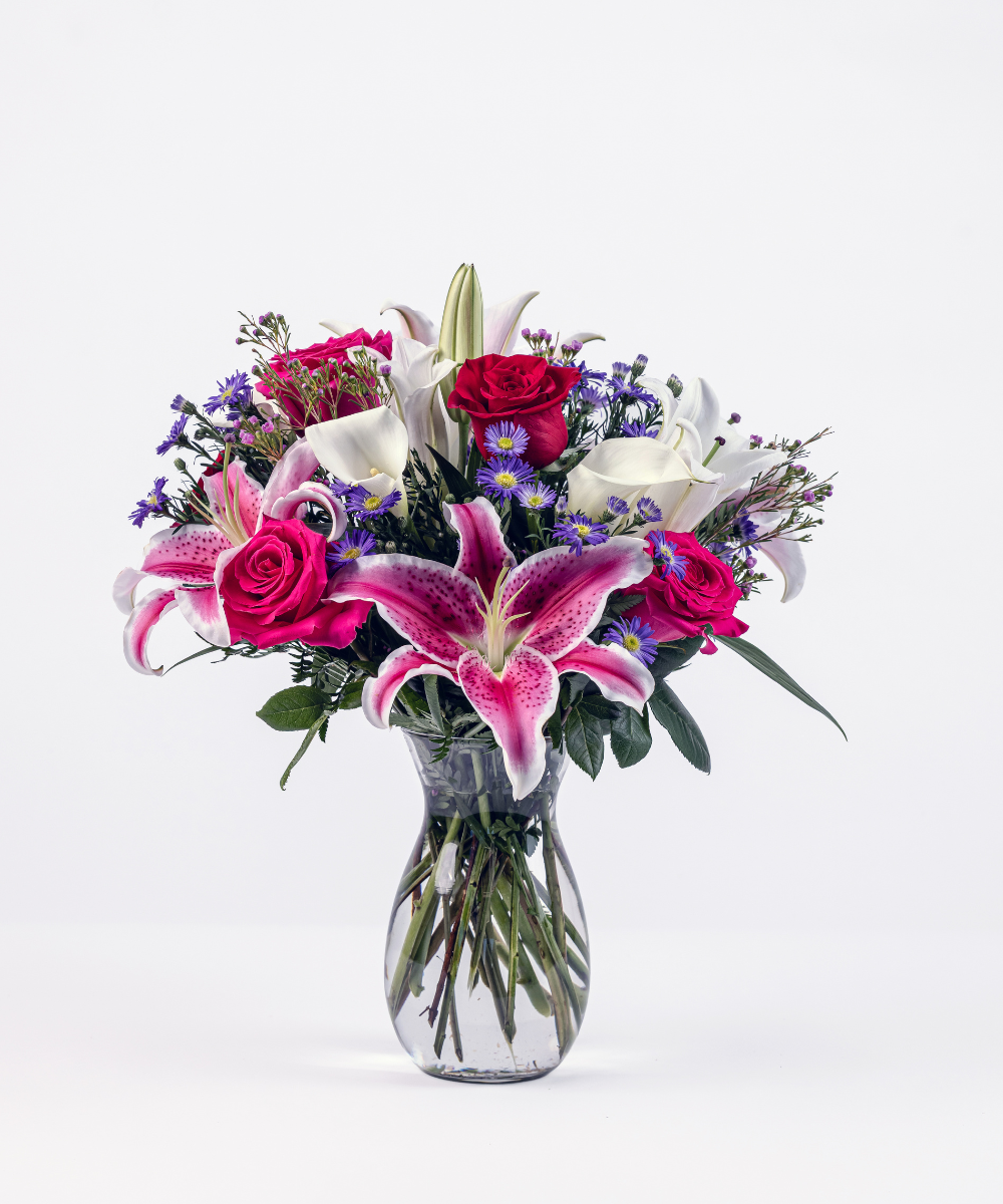 Colorful garden-style floral arrangement with lilies, roses, mini calla lilies, and purple asters in a Jordan vase
