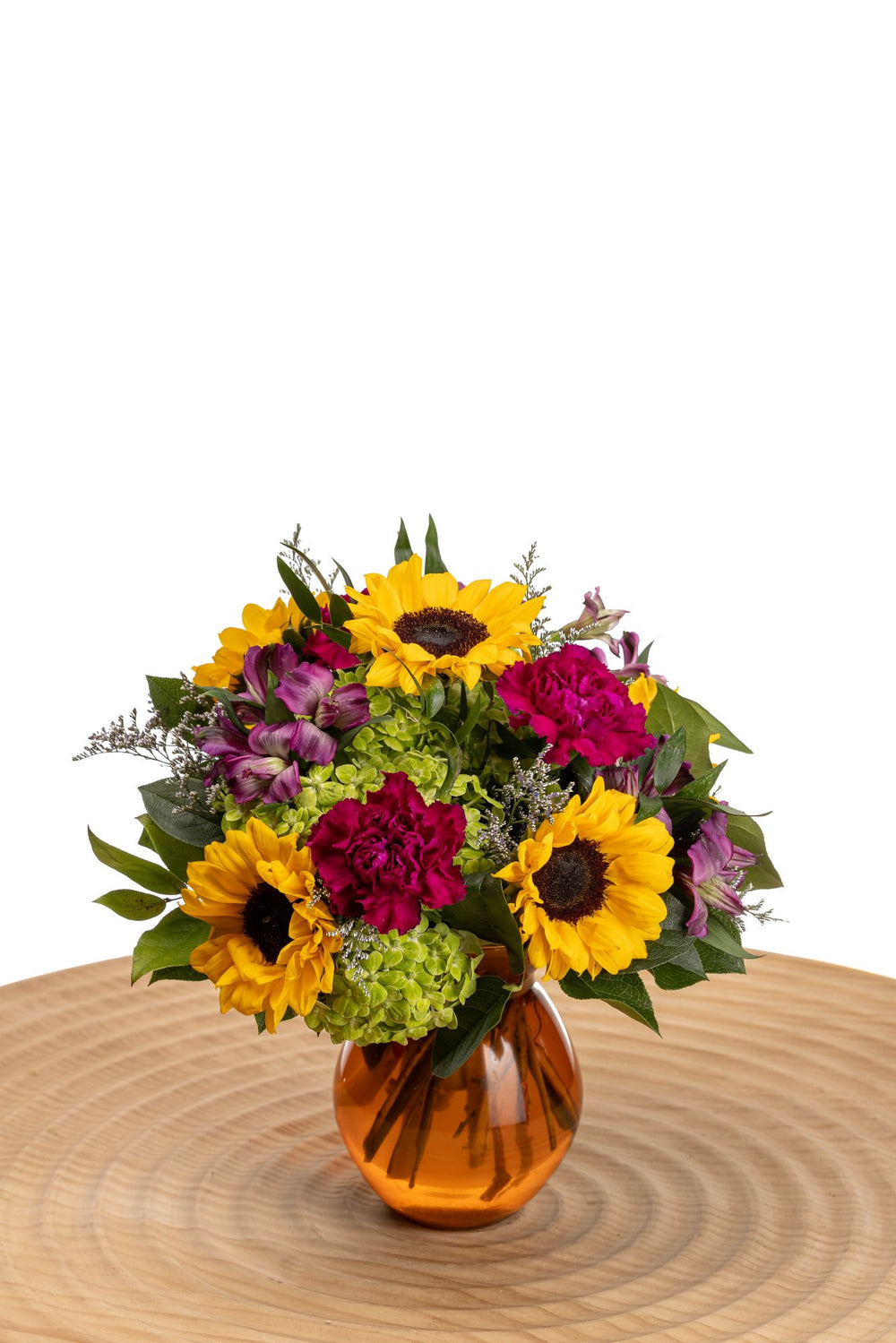 Sunflower Spice presents petite sunflowers, purple alstroemeria, green hydrangea, purple carnations, and limonium in a marigold ceramic vase.