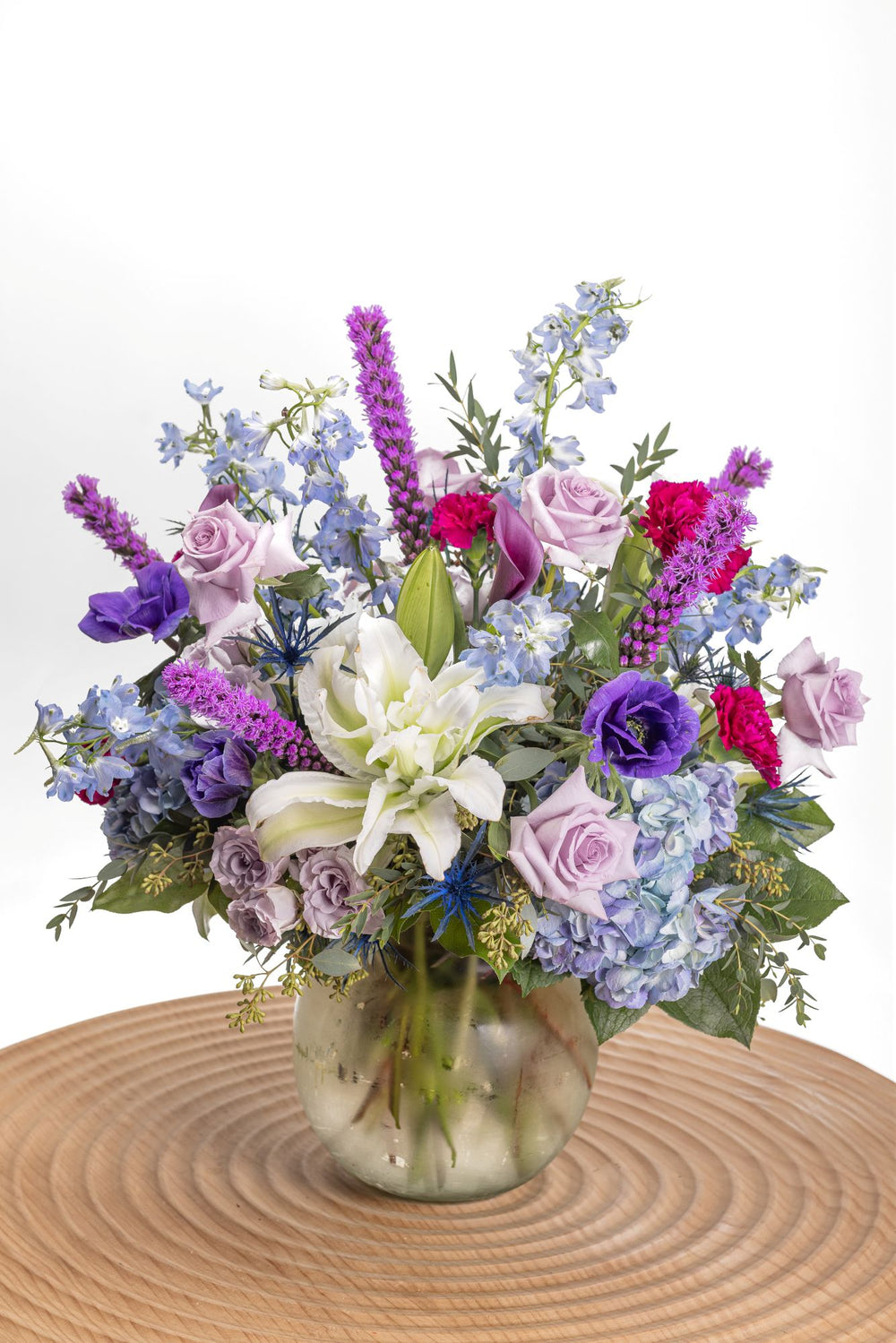 Ultra Violet features hydrangeas, lavender spray roses, blue anemones, tinted thistle, liatris, delphinium, mini calla lilies, ruffled purple carnations, double white lily roses with a variety of fresh greenery in a glass vase.